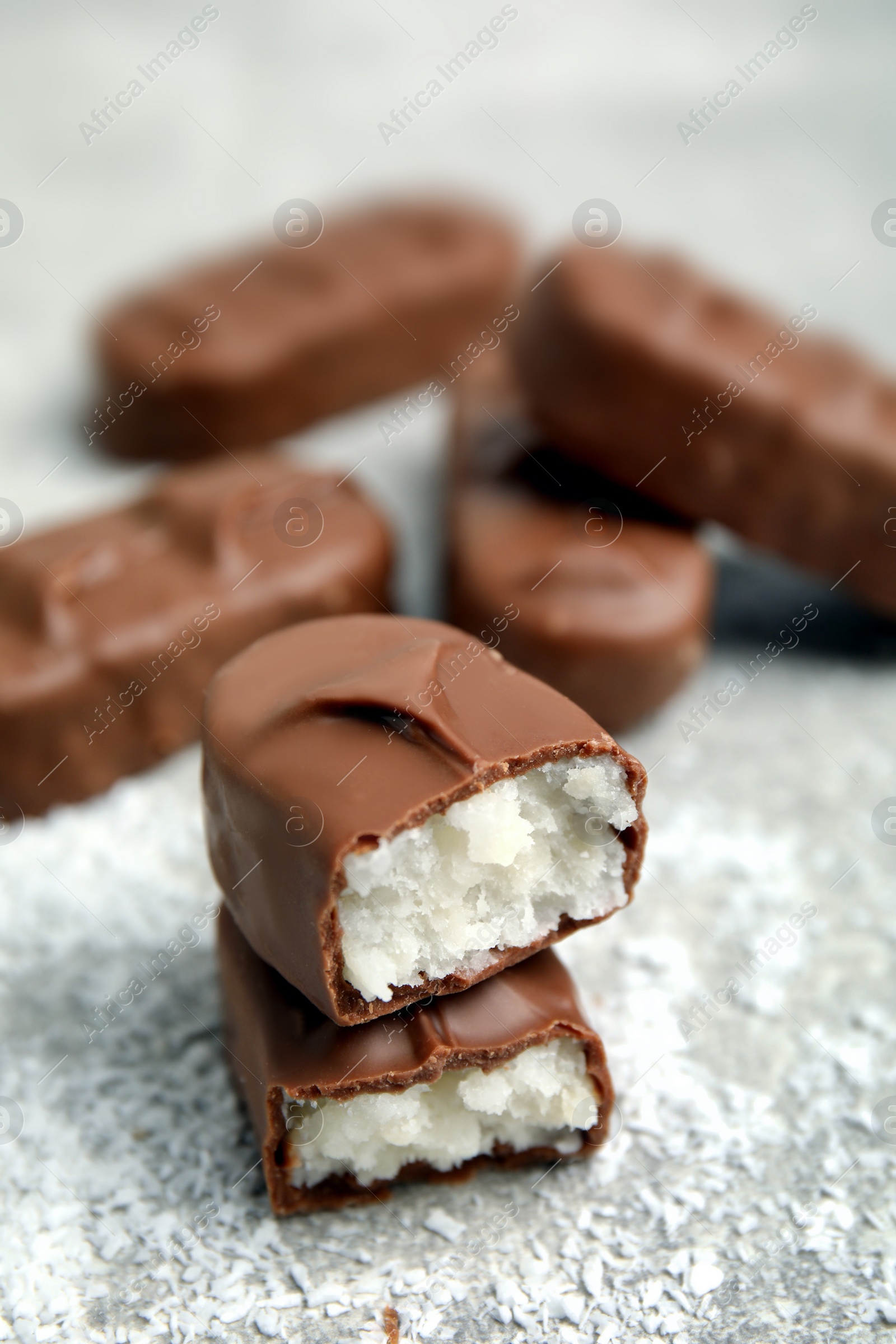 Photo of Delicious milk chocolate candy bars with coconut filling on grey table, closeup