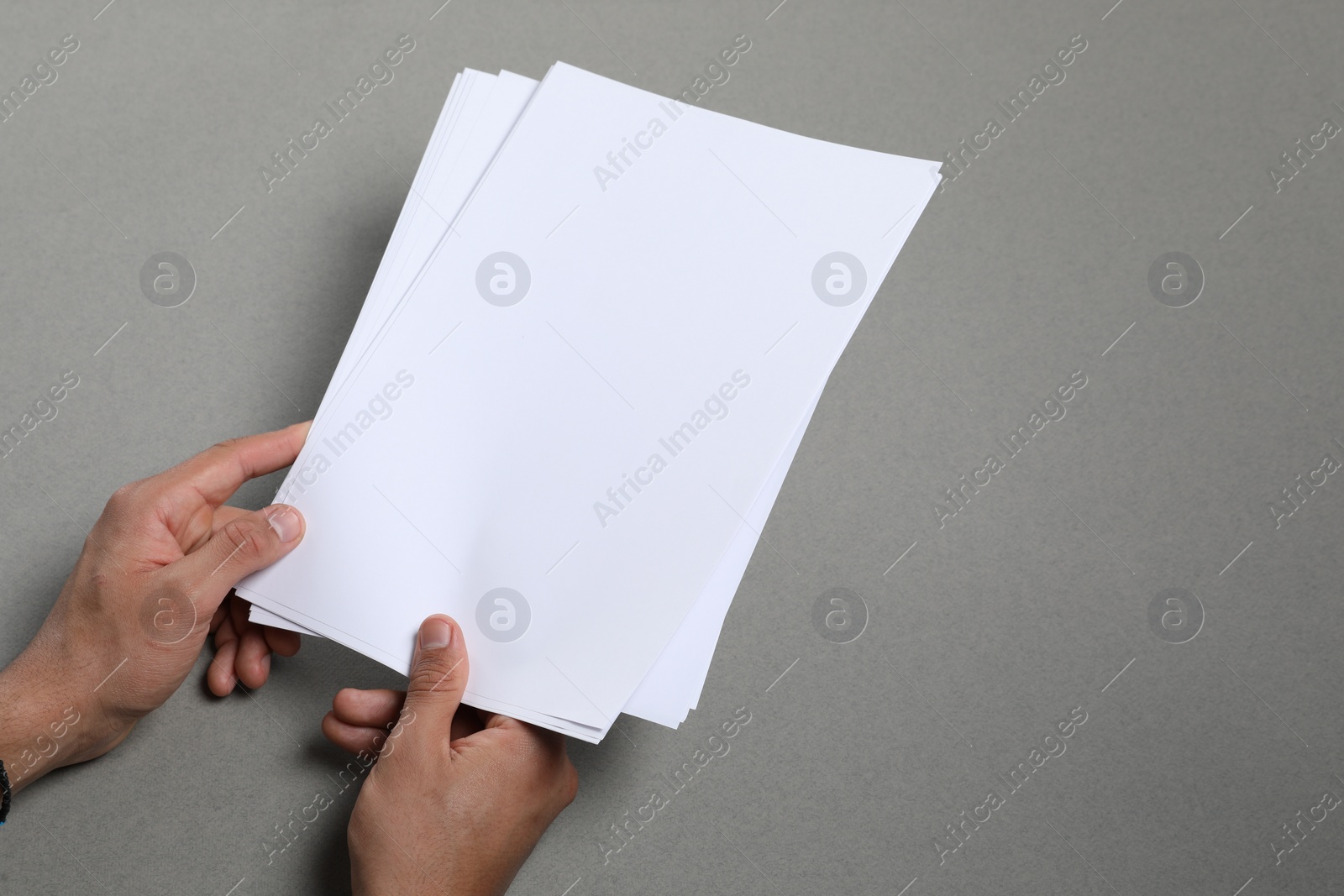 Photo of Man holding sheets of paper on grey background, closeup. Mockup for design