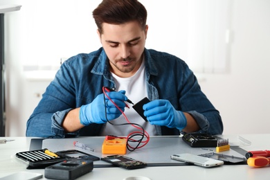 Photo of Technician checking broken smartphone at table in repair shop