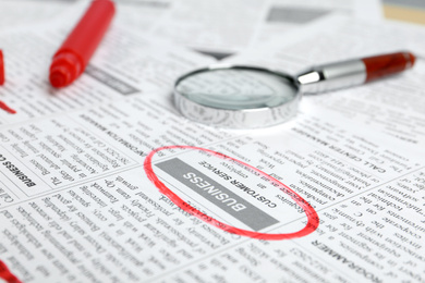 Photo of Newspaper with marked advertisement and magnifying glass. Search concept
