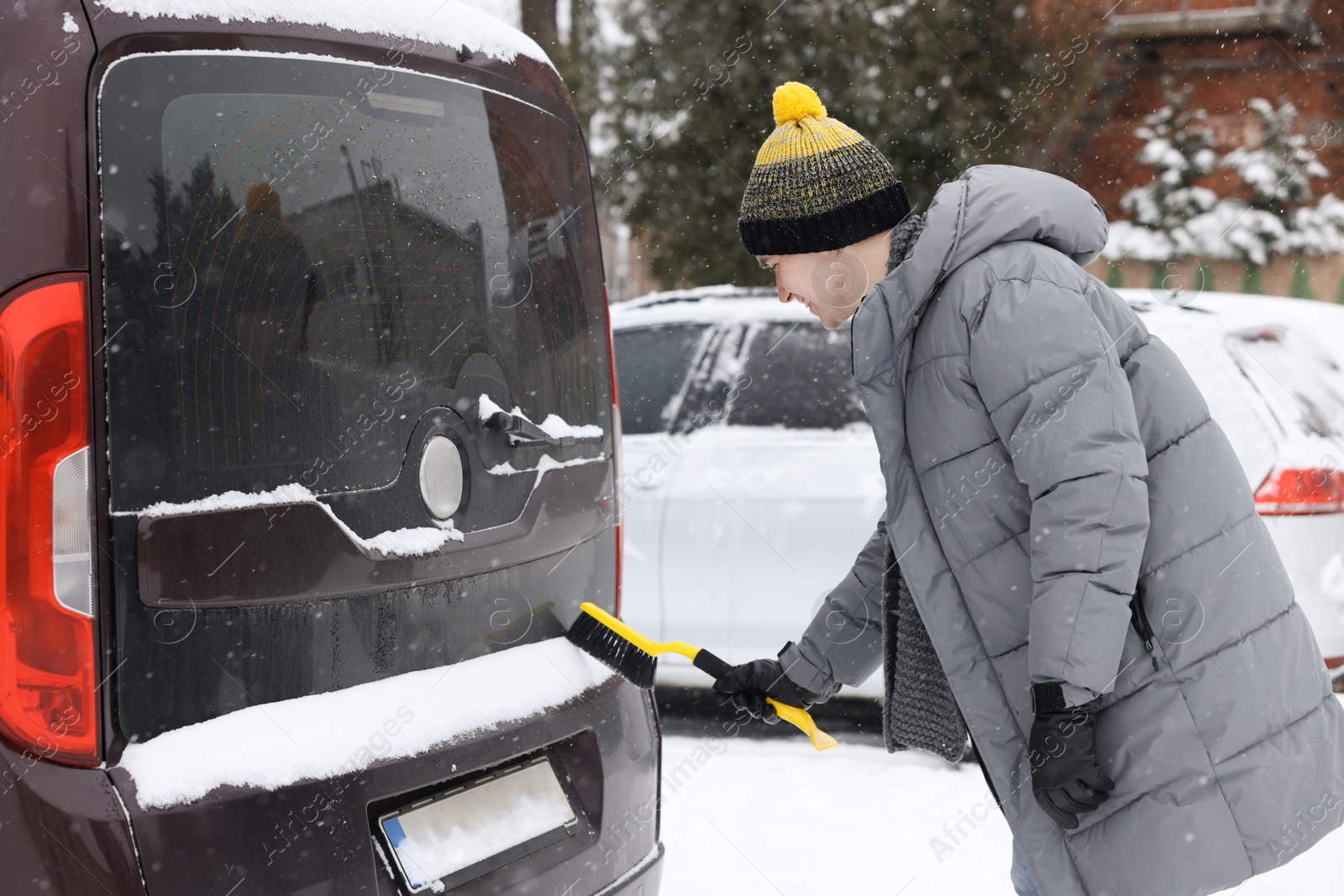 Photo of Man cleaning snow from car with brush outdoors