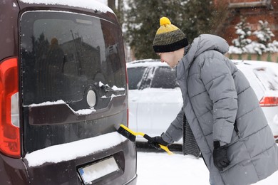 Photo of Man cleaning snow from car with brush outdoors