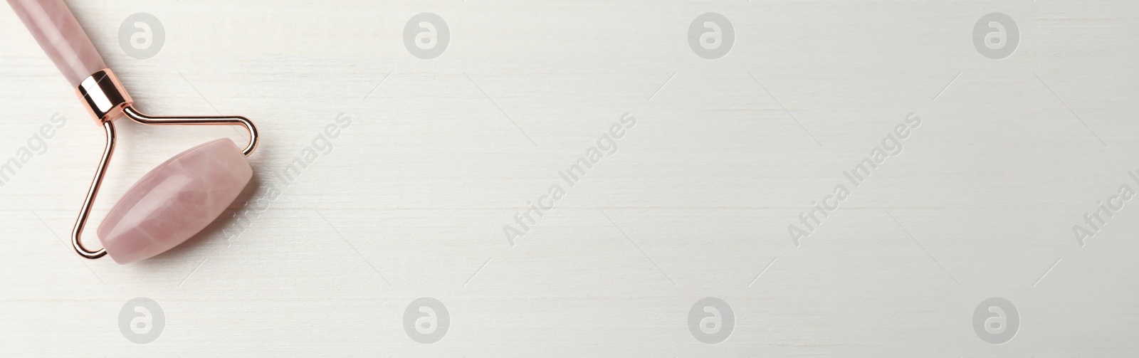 Image of Natural quartz face roller on white wooden background, top view with space for text. Banner design