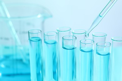 Dripping liquid from pipette into test tube on blurred background, closeup. Laboratory analysis