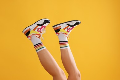 Woman wearing stylish sneakers on yellow background, closeup