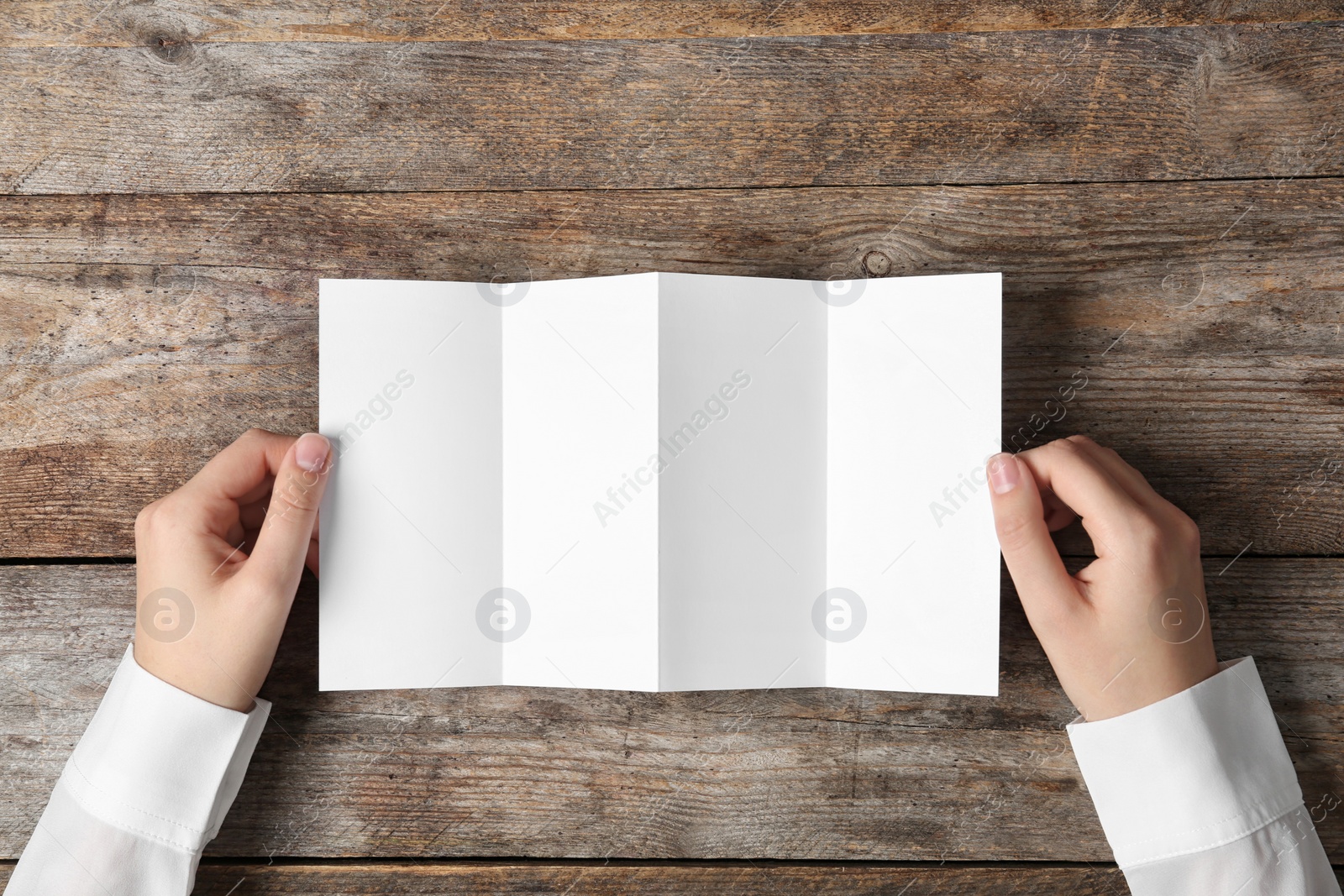 Photo of Woman holding blank brochure mock up on wooden table, top view