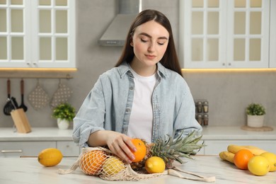 Woman with string bag of fresh fruits at light marble table in kitchen