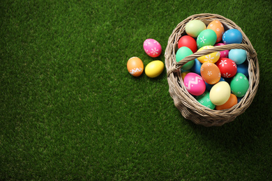 Photo of Colorful Easter eggs in basket on green grass, above view. Space for text