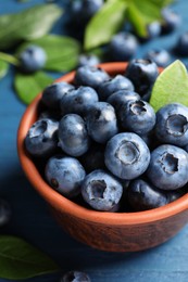 Tasty fresh blueberries in bowl on blue table, closeup