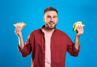 Young man with tasty sandwiches on light blue background