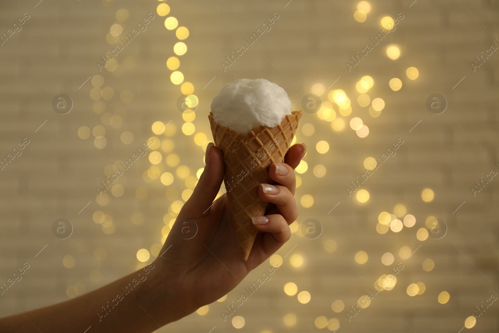 Photo of Woman holding waffle cone with cotton candy against blurred lights, closeup