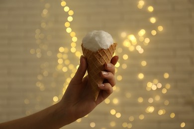 Woman holding waffle cone with cotton candy against blurred lights, closeup