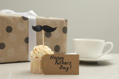 Photo of Card with phrase Happy Father's Day and delicious cupcake with mustache topper on light table