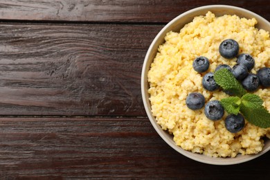 Photo of Tasty millet porridge with blueberries and mint in bowl on wooden table, top view. Space for text