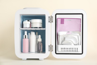 Photo of Open cosmetic refrigerator with skin care products on beige background