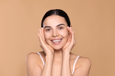 Photo of Beautiful young woman with cream on skin under eye against beige background