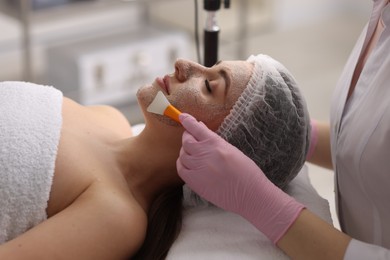 Photo of Cosmetologist applying mask on woman's face in clinic, closeup