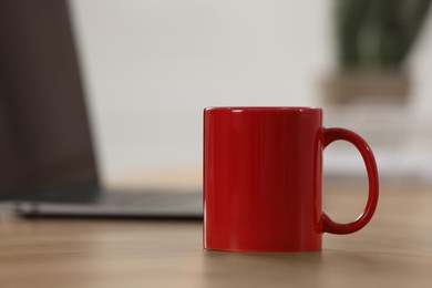 Photo of Red ceramic mug on wooden table at workplace. Space for text