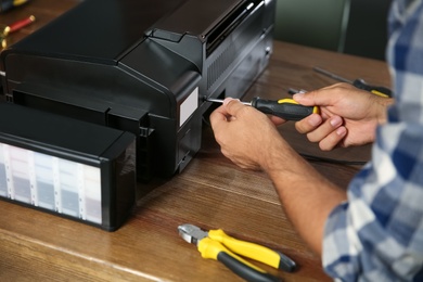 Repairman with screwdriver fixing modern printer indoors, closeup