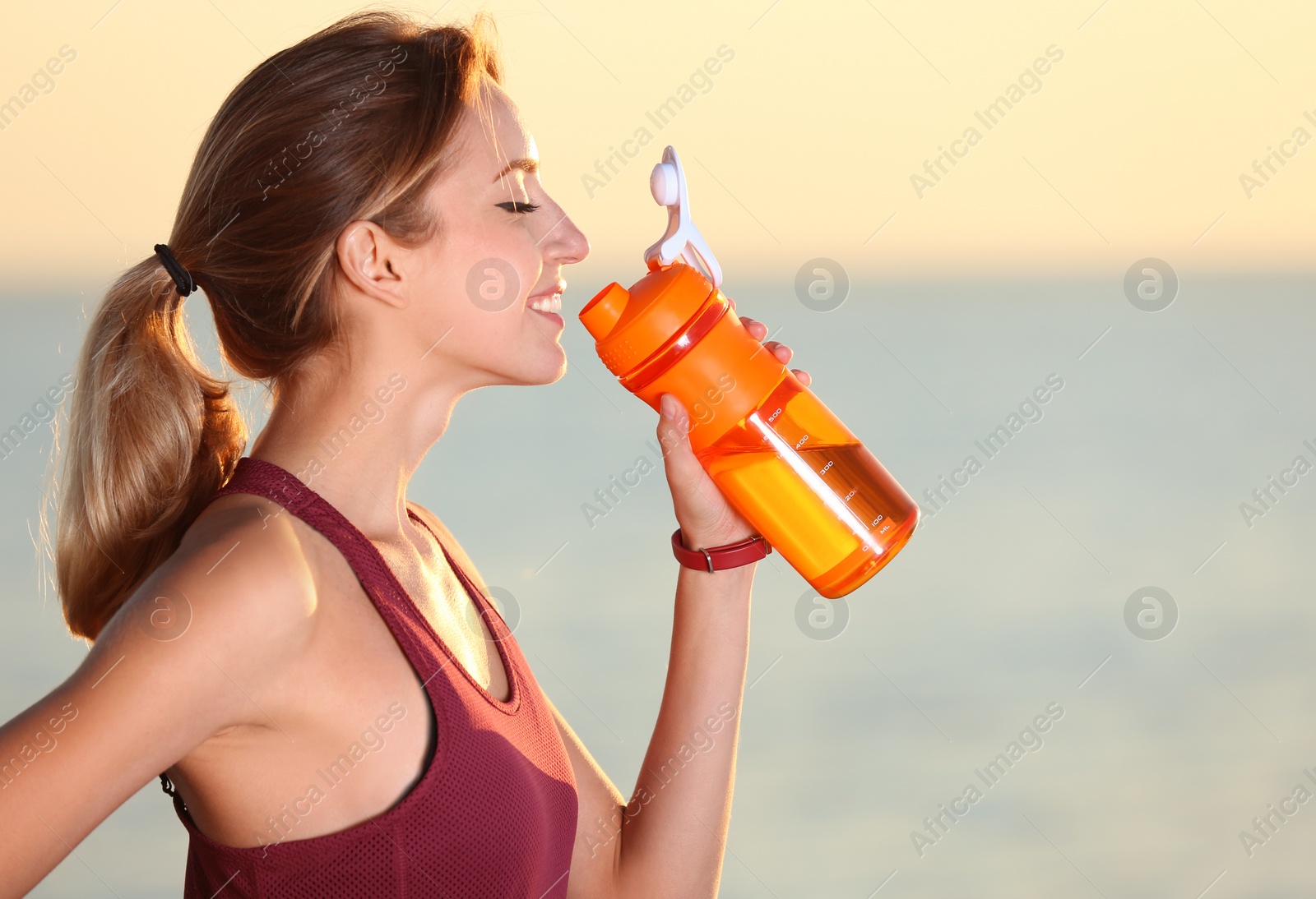 Photo of Young woman drinking water from bottle after fitness exercises near sea