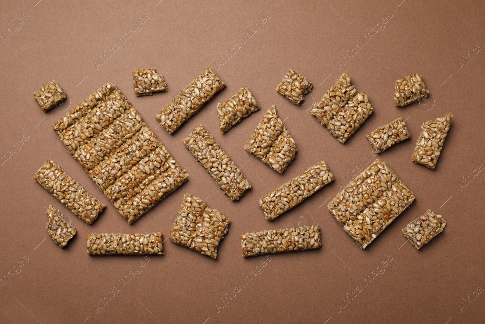 Photo of Pieces of delicious kozinaki bars on brown background, flat lay