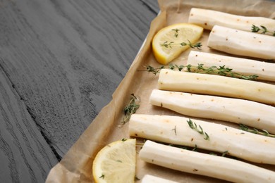 Photo of Baking tray with raw salsify roots, lemon and thyme on grey wooden table, closeup. Space for text