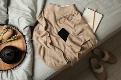 Soft cashmere sweater and tray with tea set on bed at home