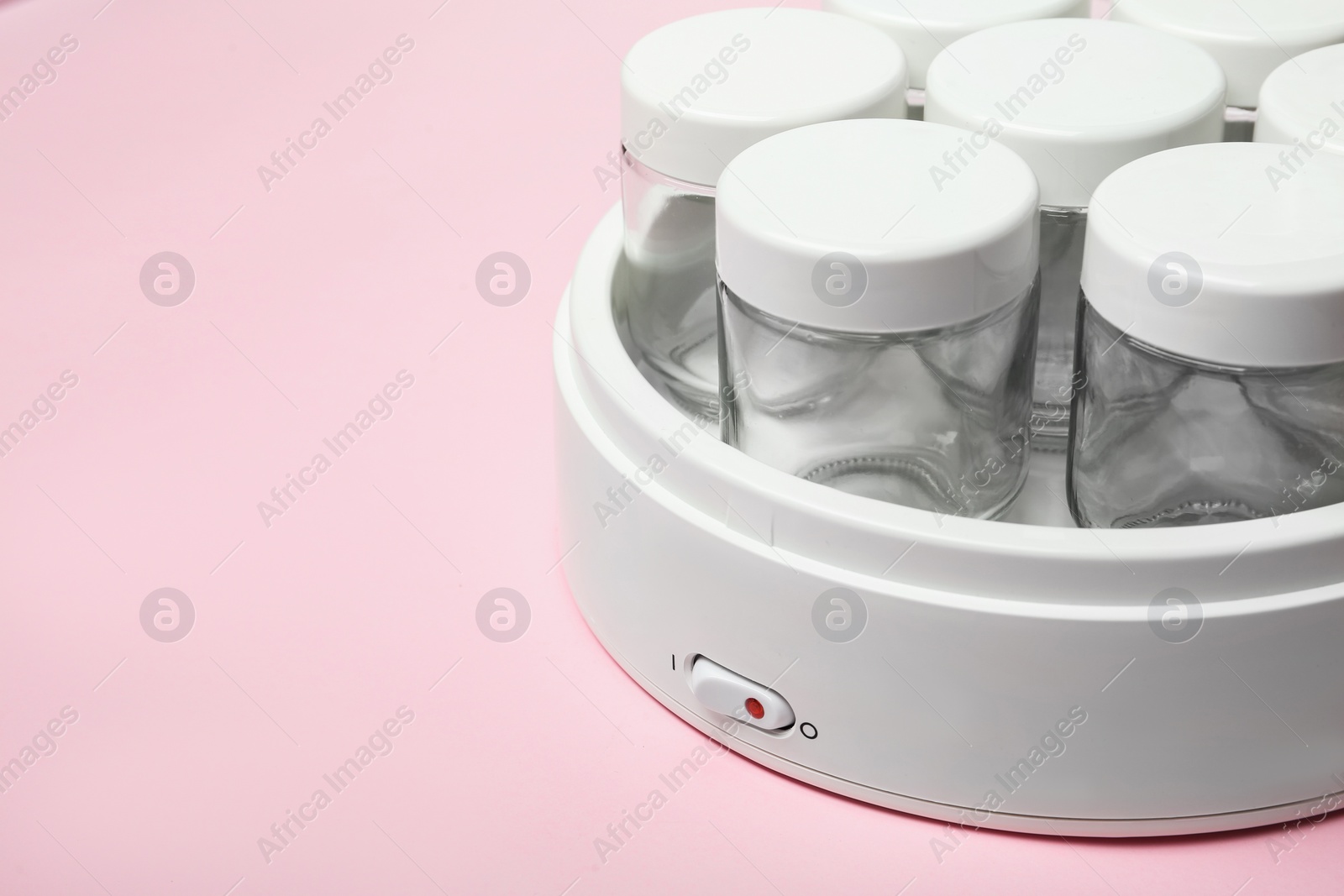 Photo of Modern yogurt maker with empty jars on pink background, closeup. Space for text