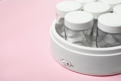 Photo of Modern yogurt maker with empty jars on pink background, closeup. Space for text