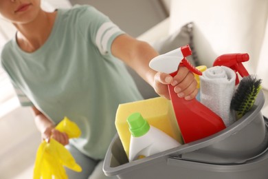 Woman taking bottle of detergent from bucket with cleaning supplies indoors, closeup