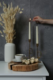 Photo of Woman lighting candle on table near grey wall indoors, closeup. Interior design