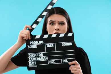 Photo of Emotional actress with clapperboard on light blue background. Film industry