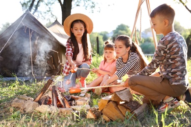 Photo of Little children frying sausages on bonfire. Summer camp