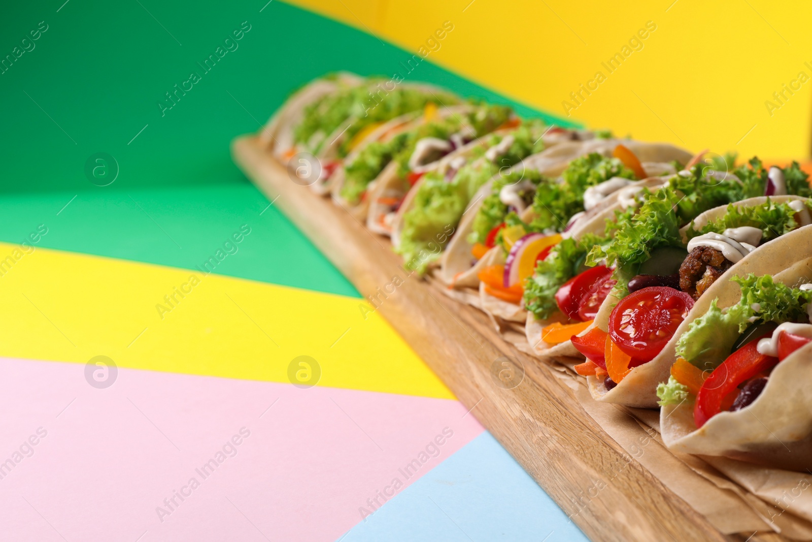 Photo of Many delicious vegetarian tacos served on color table, closeup. Space for text