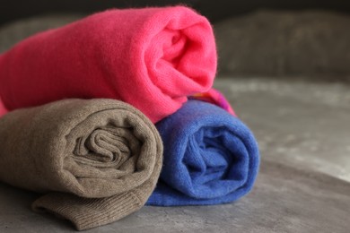 Photo of Rolled color sweaters on gray table, closeup