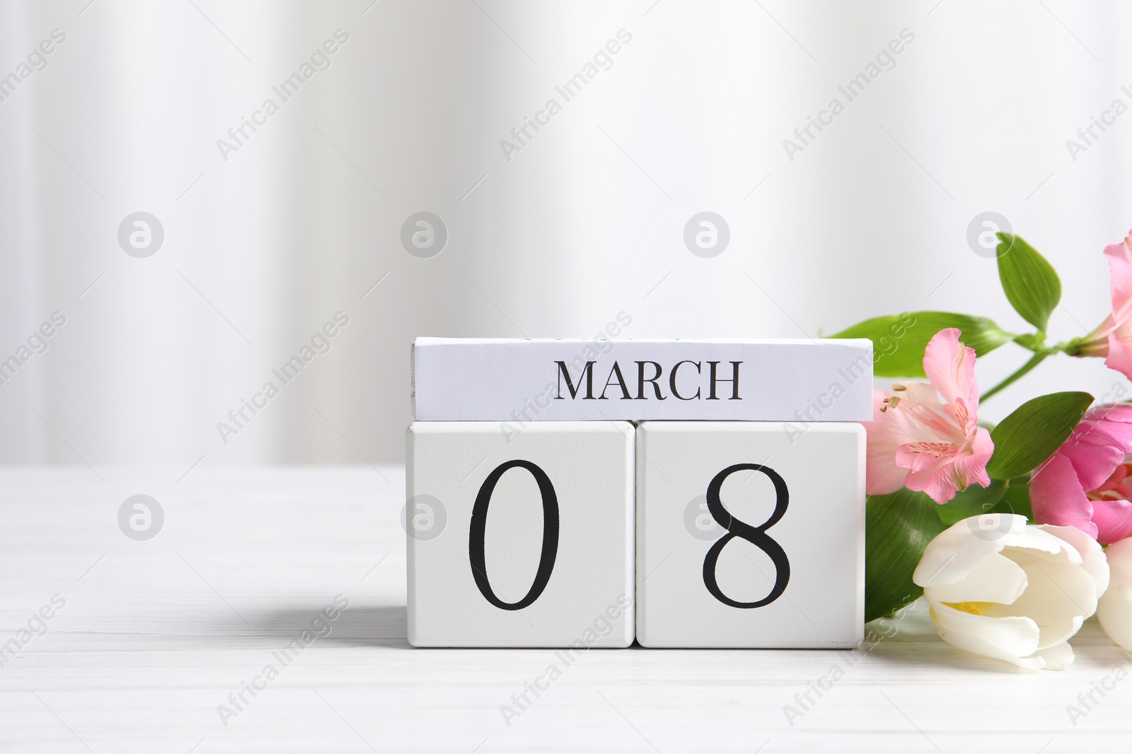 Photo of International Women's day - 8th of March. Wooden block calendar and beautiful flowers on white table, space for text