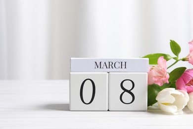 Photo of International Women's day - 8th of March. Wooden block calendar and beautiful flowers on white table, space for text