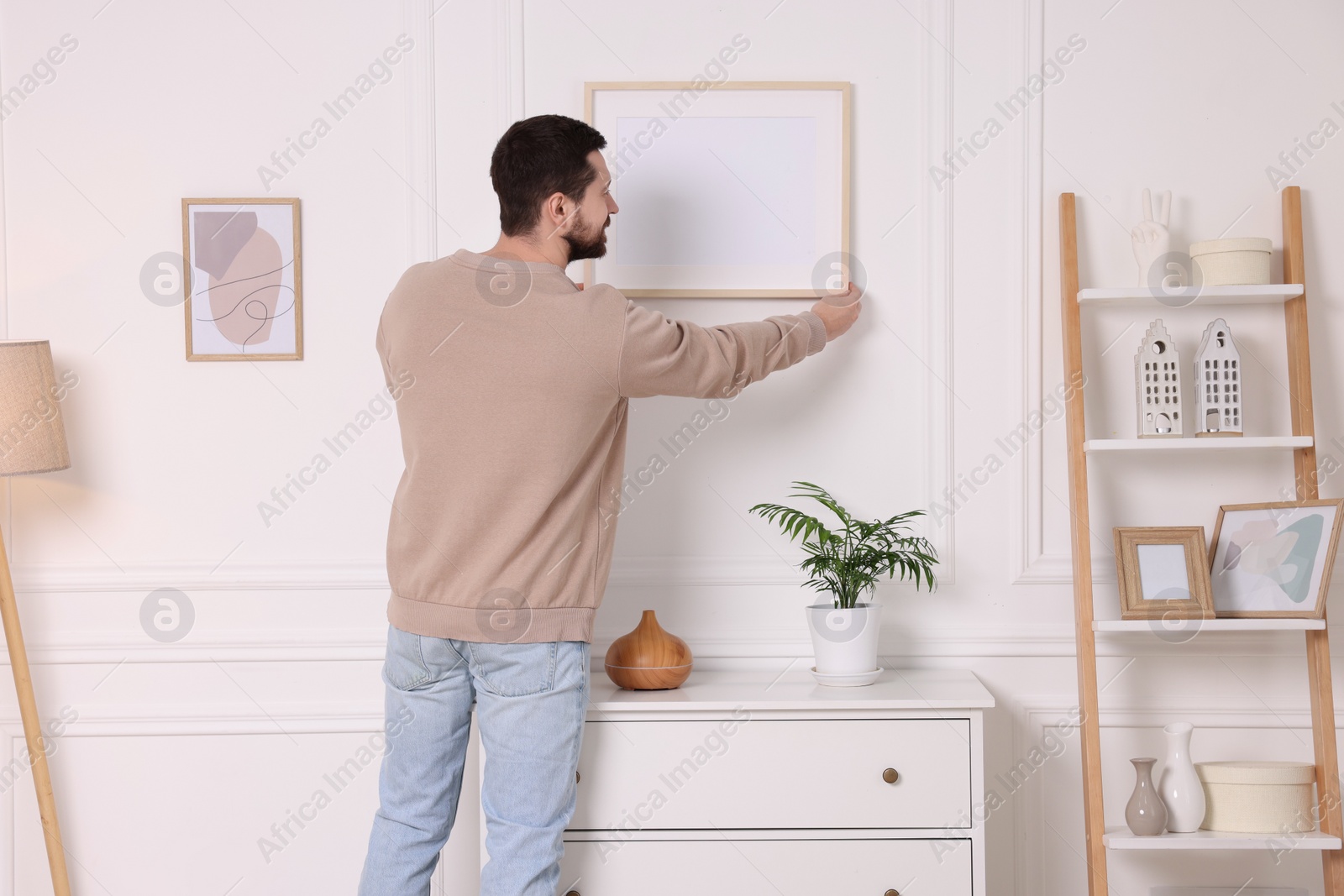 Photo of Man hanging picture frame on white wall at home