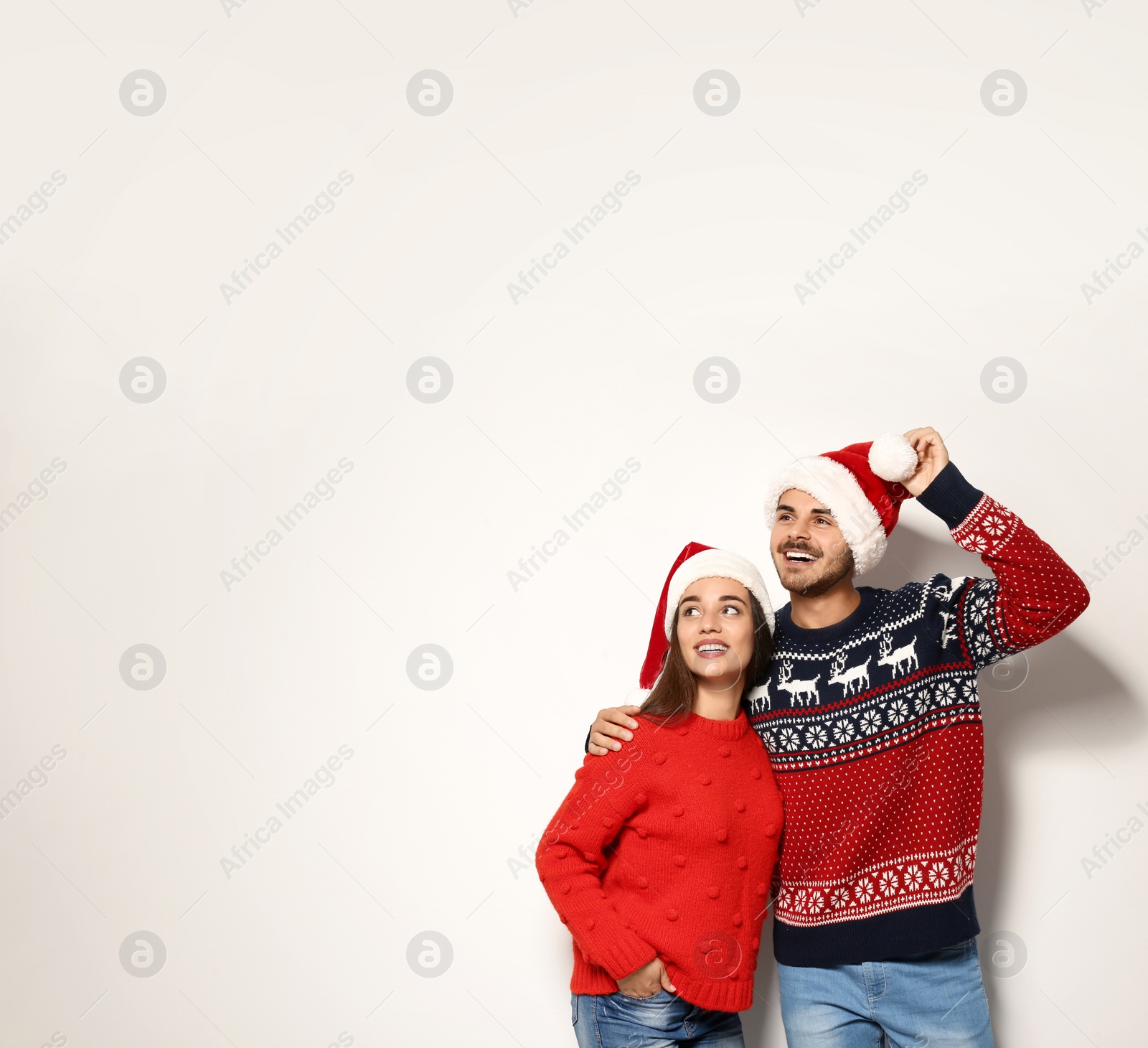 Photo of Young couple in warm sweaters and Christmas hats on white background. Space for text