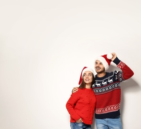 Photo of Young couple in warm sweaters and Christmas hats on white background. Space for text