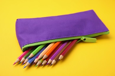 Photo of Many colorful pencils in pencil case on yellow background, closeup