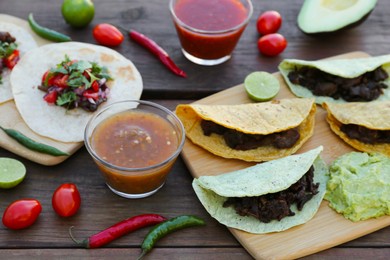 Photo of Delicious tacos and ingredients on wooden table. Mexican food