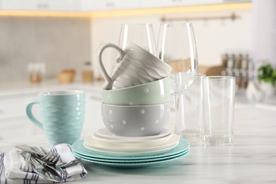 Many different clean dishware, cutlery, glasses and cups on white marble table in kitchen