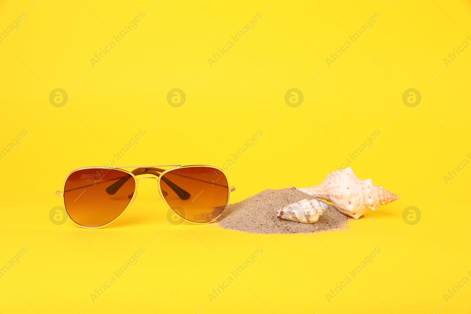 Photo of Stylish sunglasses, seashells and sand on yellow background. Space for text