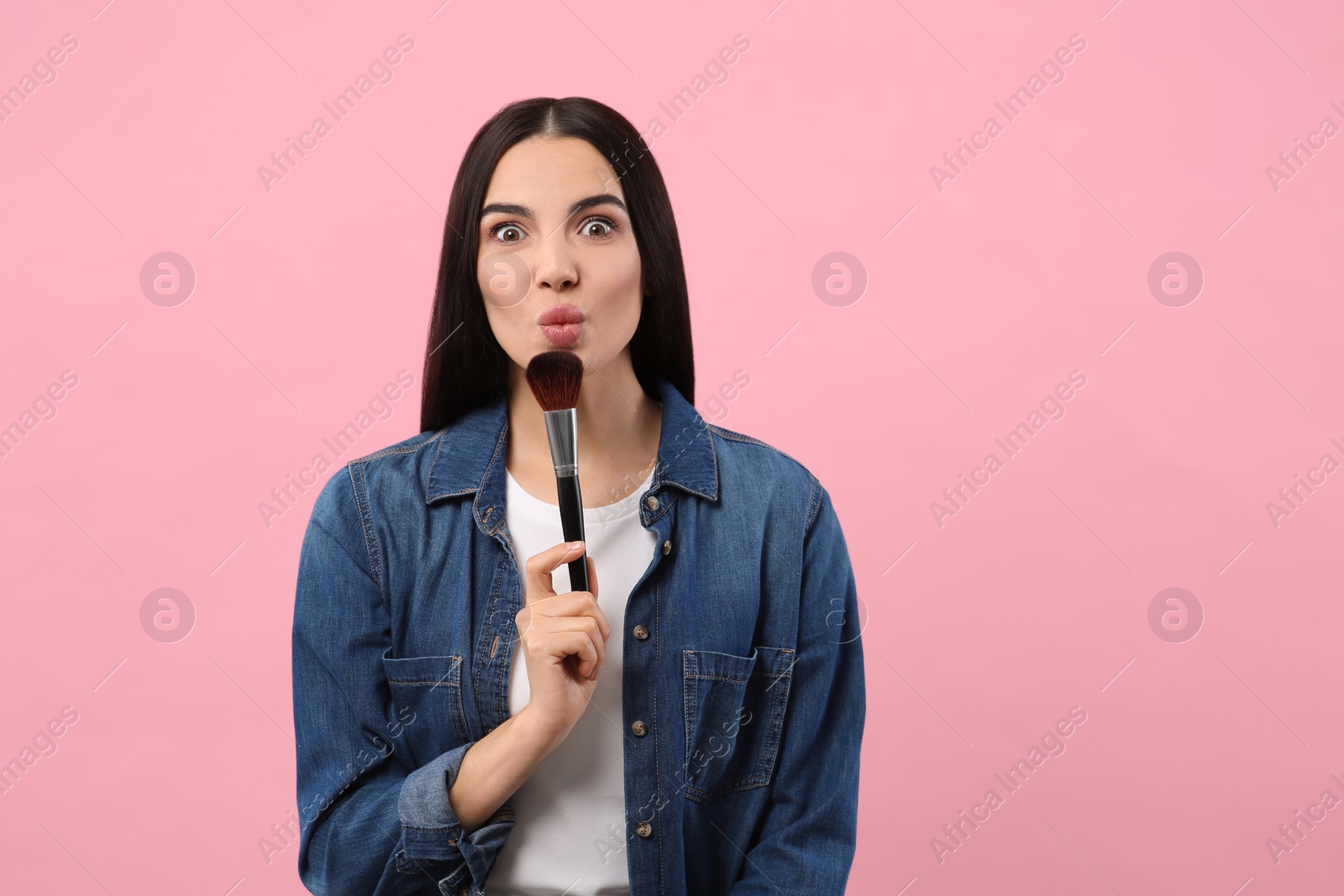 Photo of Emotional woman with makeup brush on pink background. Space for text