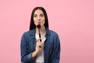 Emotional woman with makeup brush on pink background. Space for text