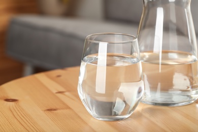 Photo of Jug and glass of water on wooden table in room, closeup with space for text. Refreshing drink