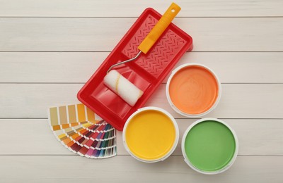 Photo of Buckets of paints, palette and decorator's tools on white wooden background, flat lay