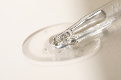 Photo of Glass pipette and transparent liquid on beige background, closeup