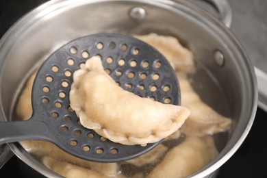 Dumpling (varenyk) with cottage cheese on skimmer over pot, closeup